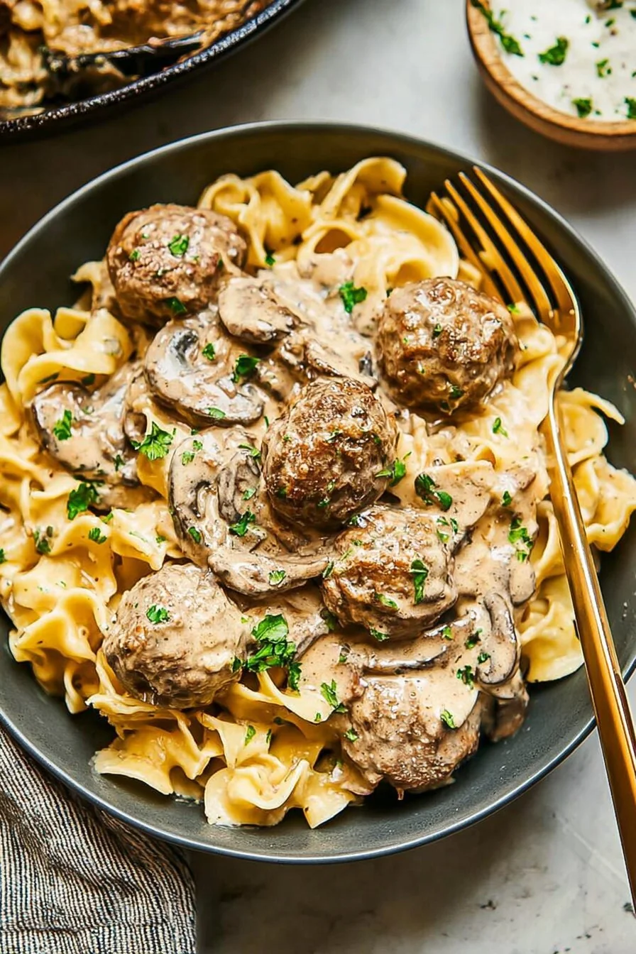 A bowl of juicy meatballs smothered in creamy stroganoff sauce over egg noodles